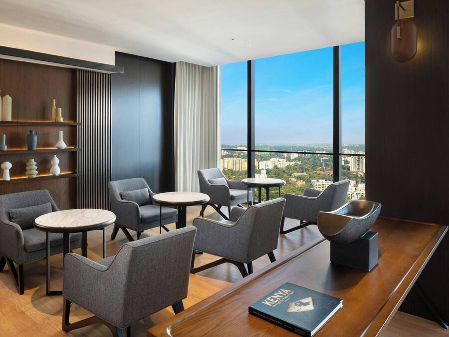 A modern lounge with grey upholstered chairs, a wooden coffee table, and a bookshelf with decorative items.