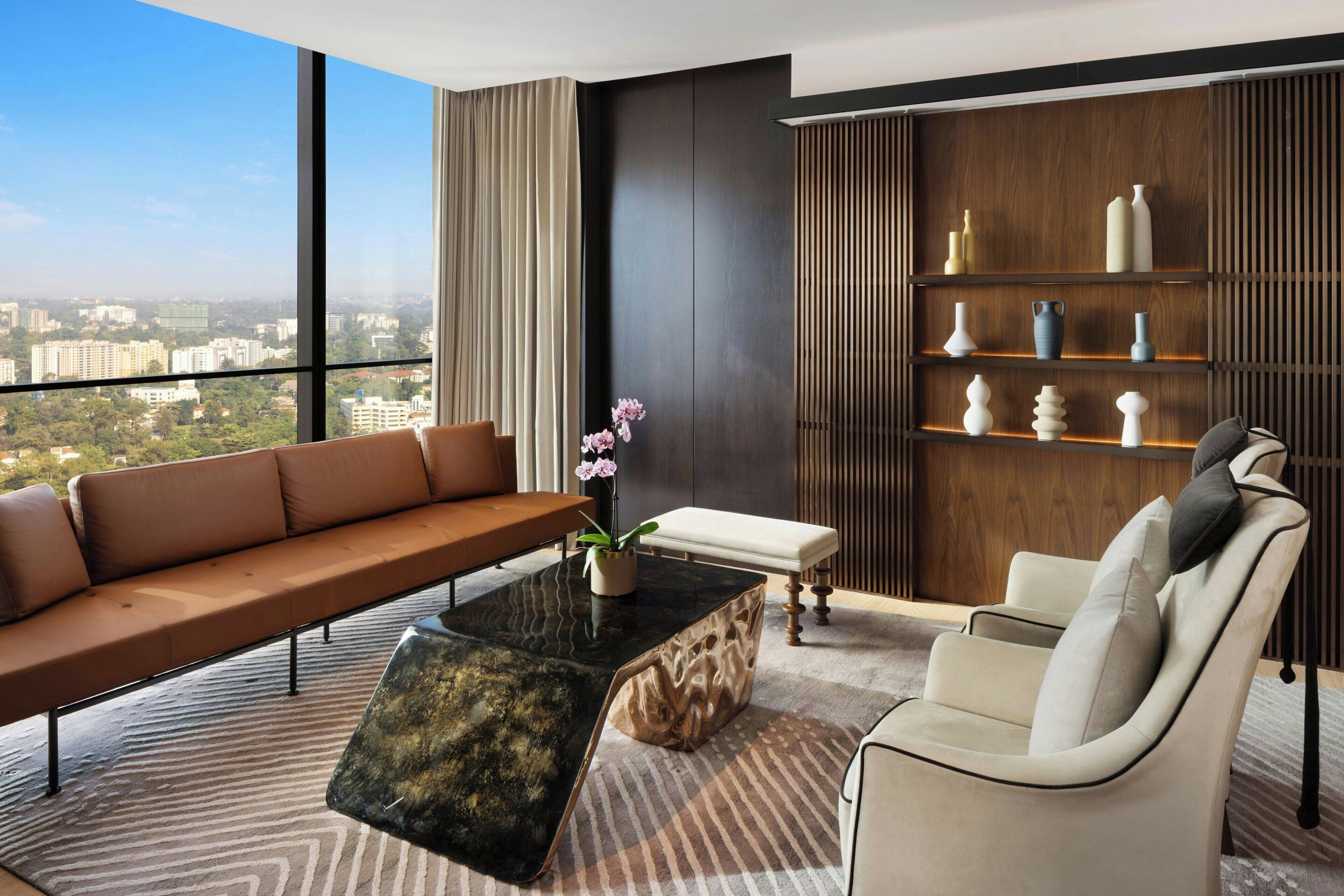 Ein modernes Wohnzimmer mit Sofa, Sessel und Couchtisch, einem Holzregal und Blick auf die Stadt.