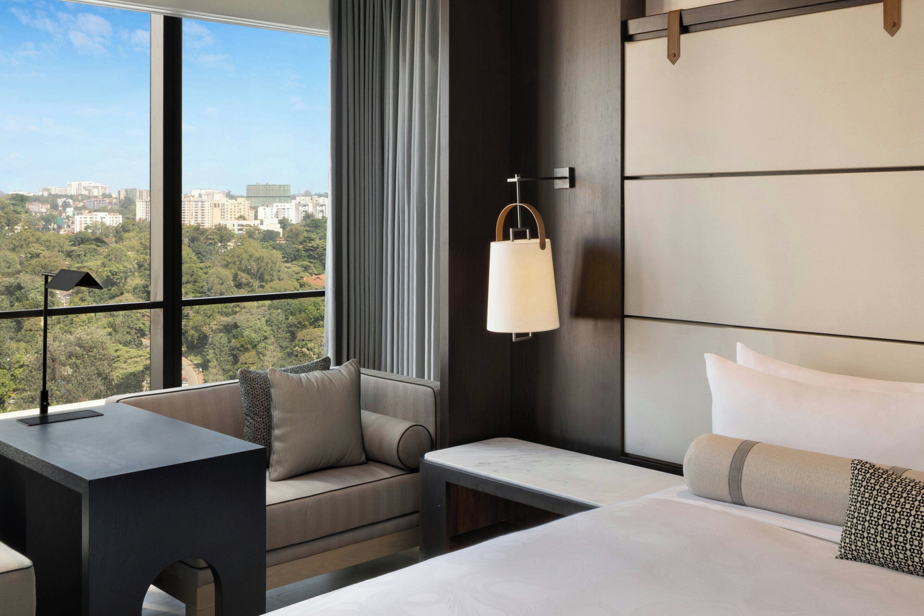 Une chambre d’hôtel avec une grande fenêtre, un canapé, un lit et une table de chevet.