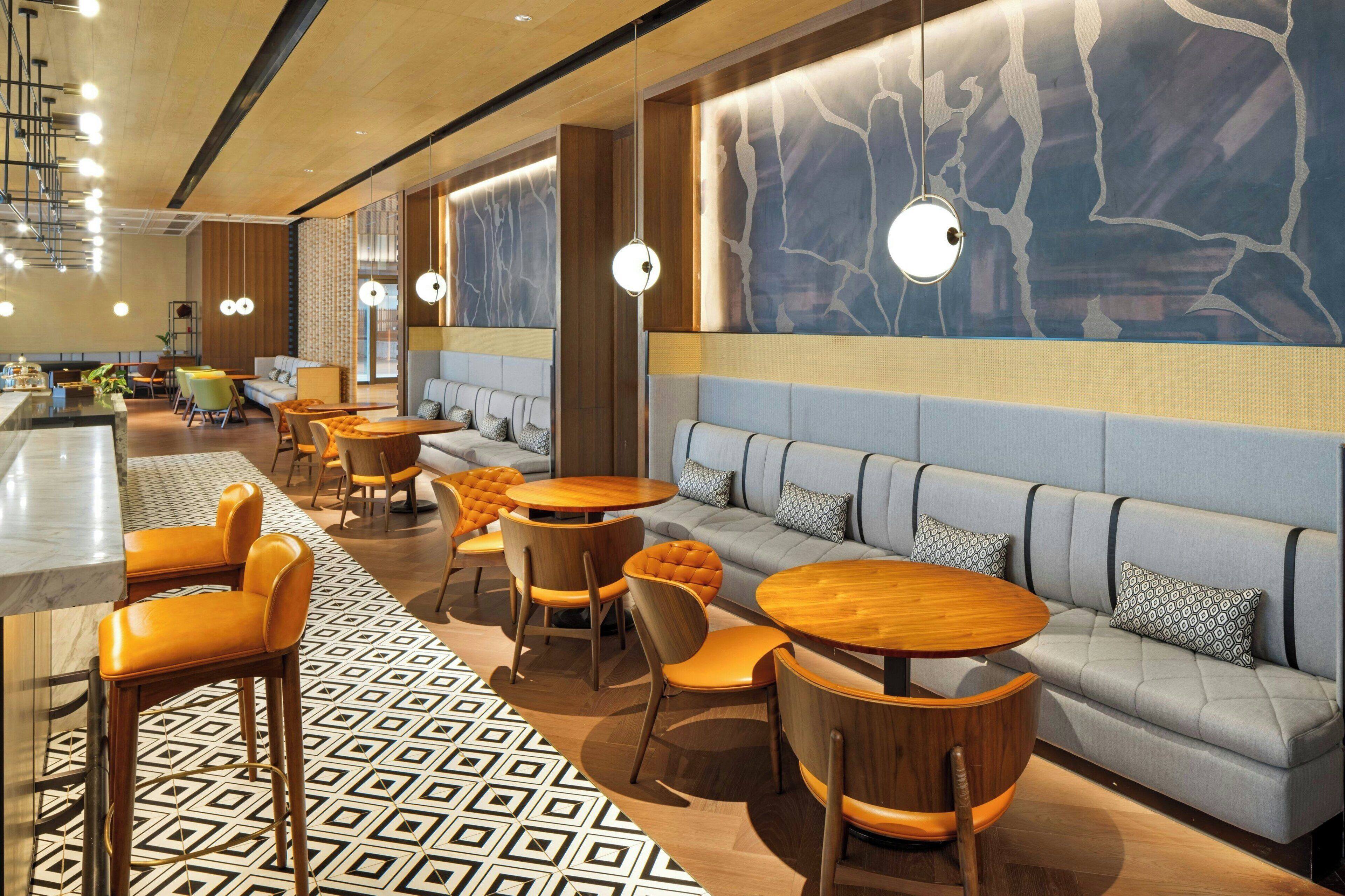 A modern restaurant interior with round tables, cushioned seating, and a patterned floor.