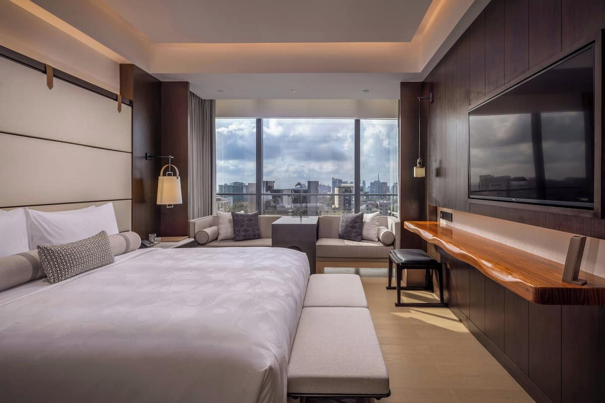 Ein modernes Hotelzimmer mit einem großen Bett, einer Sitzecke, einem Fernseher und Blick auf die Stadt.