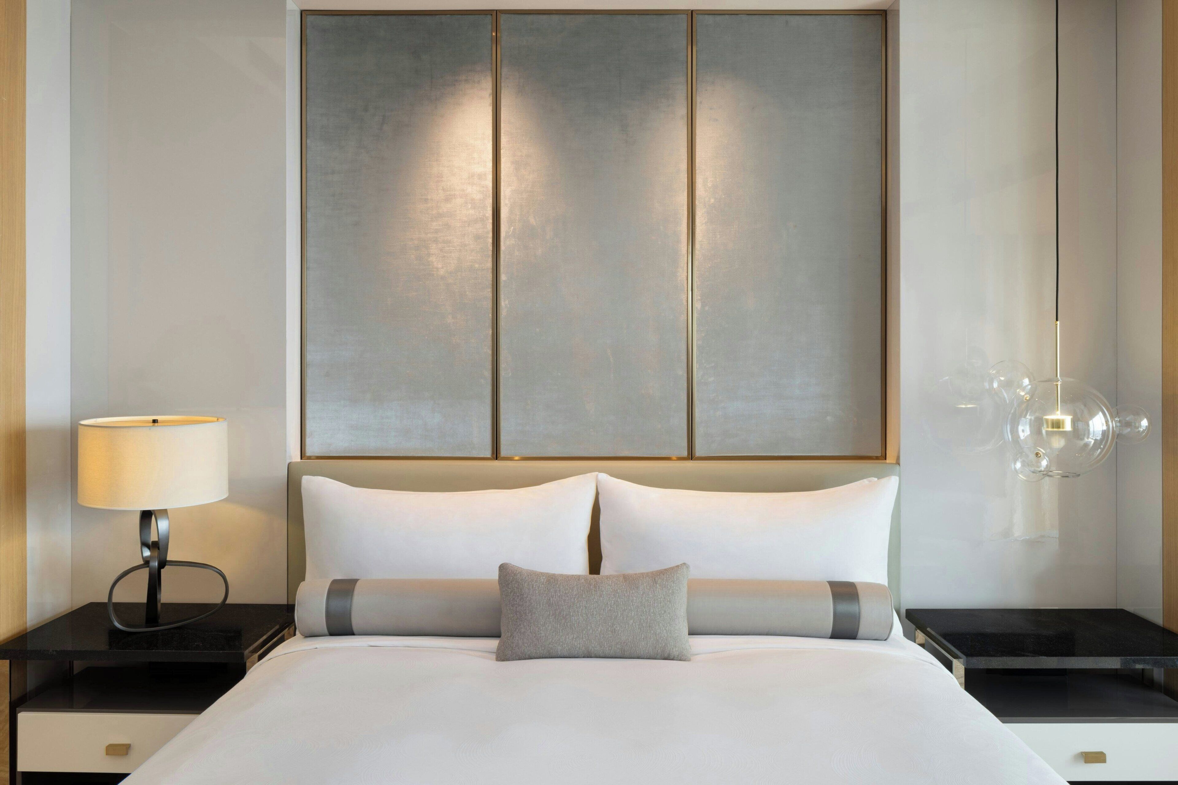 A modern hotel room with a large bed, a bedside lamp, a nightstand, and a wall-mounted light fixture.