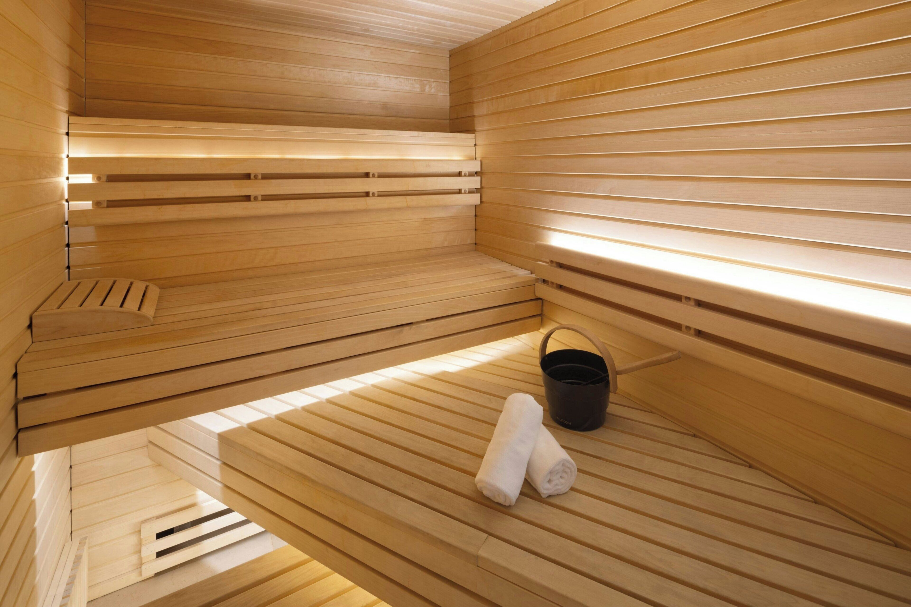 A sauna with wooden benches, a black bucket, and rolled towels.