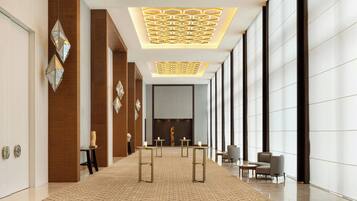 Un moderno vestíbulo de hotel con alfombra estampada, decoración de pared geométrica y una zona de estar central con mesas y sillas.