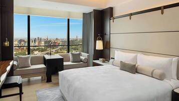 Une chambre d’hôtel moderne dotée d’un grand lit, d’un canapé, d’un bureau et offrant une vue sur le paysage urbain grâce à de grandes fenêtres.