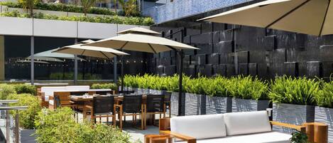 An outdoor seating area with wooden furniture, white cushions, and beige umbrellas.
