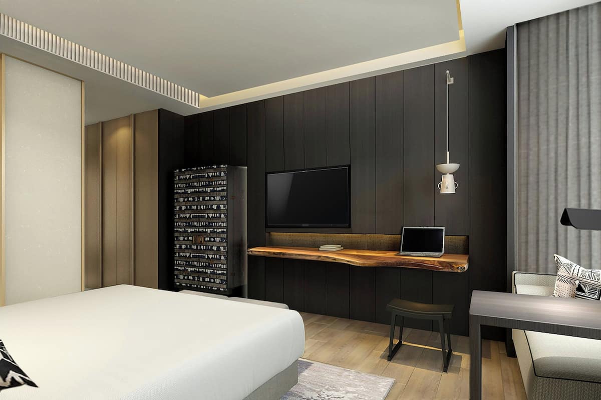 Ein modernes Hotelzimmer mit Bett, Schreibtisch mit Laptop, Fernseher und Bücherregal.