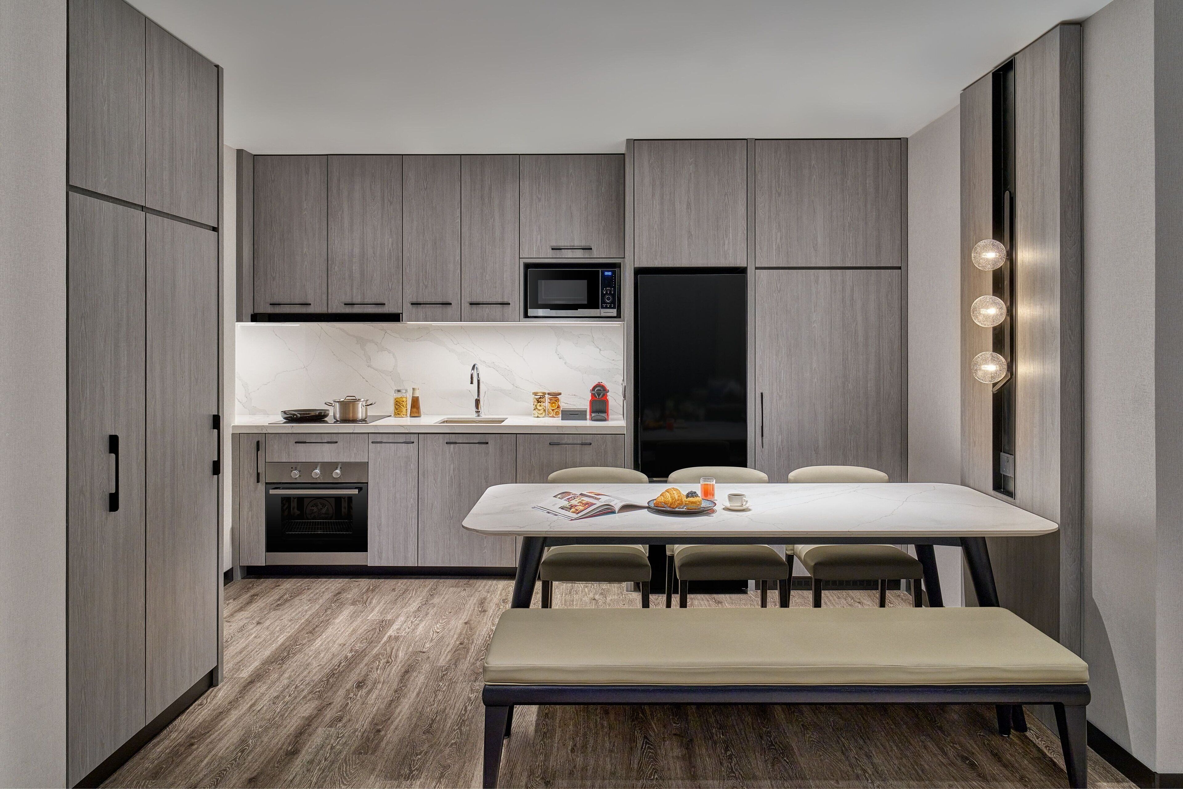 A modern kitchen with grey cabinets, a black refrigerator, a microwave, and a dining area with a table and chairs.