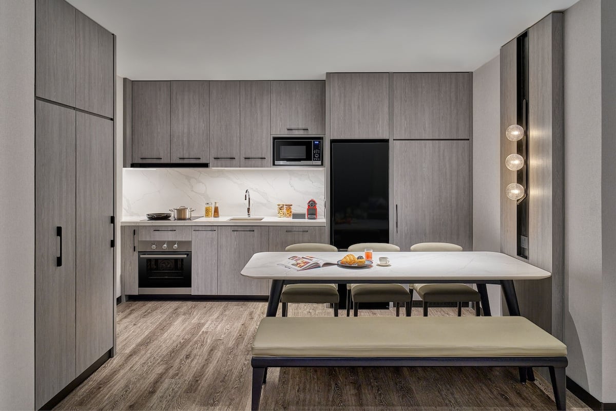 A modern kitchen with grey cabinets, a black refrigerator, a microwave, and a dining area with a table and chairs.