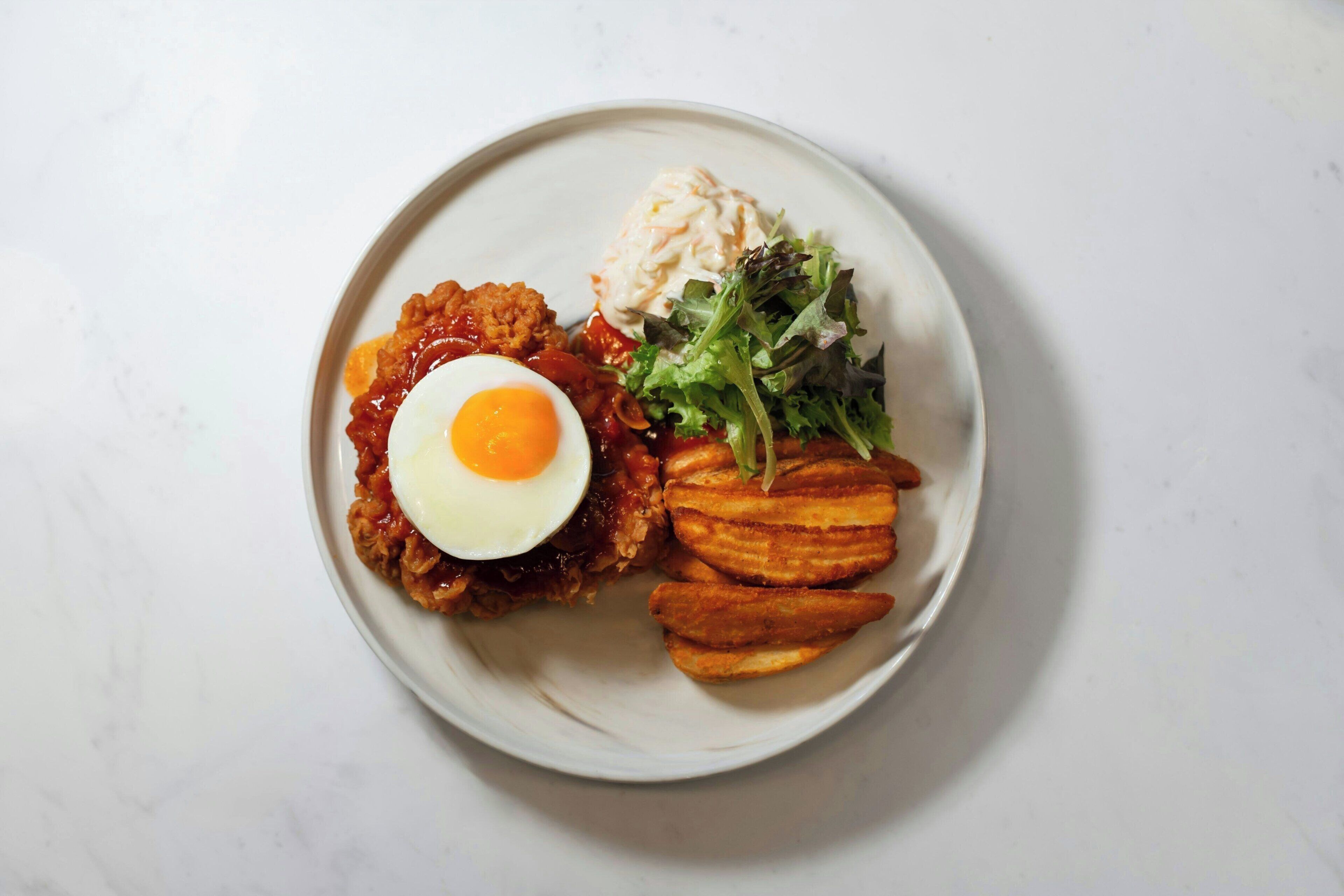 A plate with a fried egg, a slice of meat, a side of potatoes, and a salad.