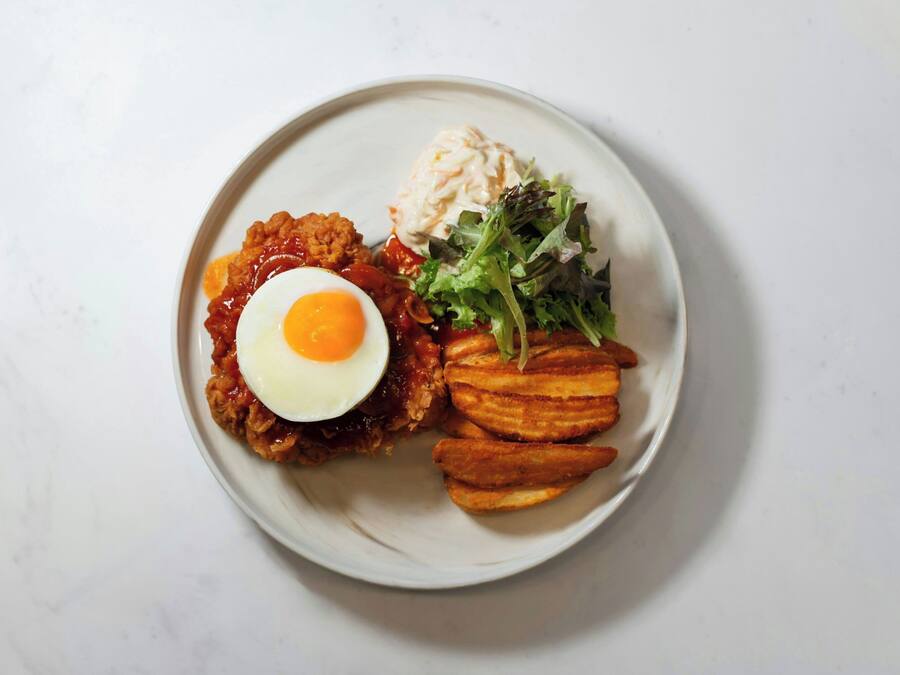 A plate with a fried egg, a slice of meat, a side of potatoes, and a salad.