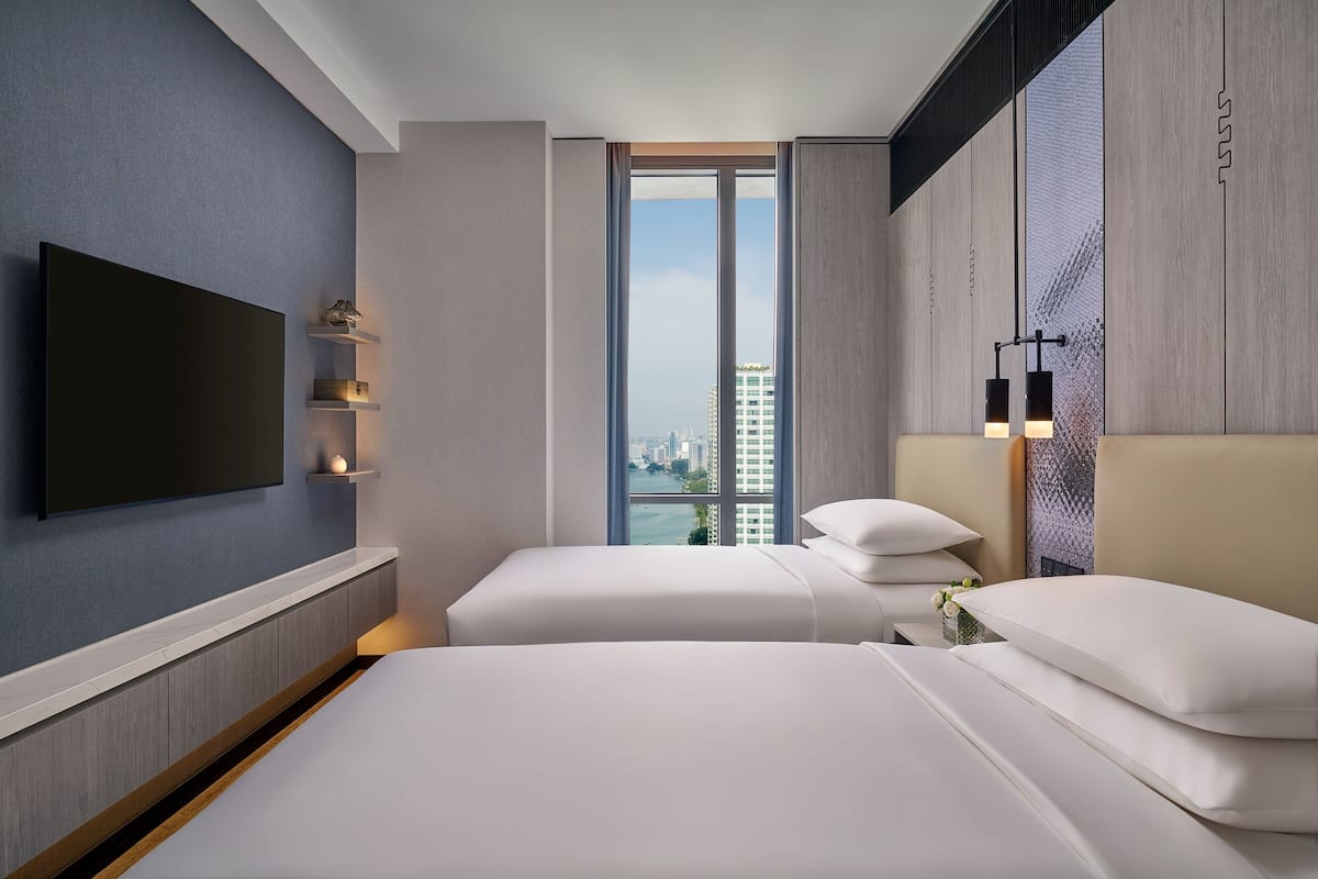 A modern hotel room with a large bed, a TV mounted on the wall, and a city view through the window.