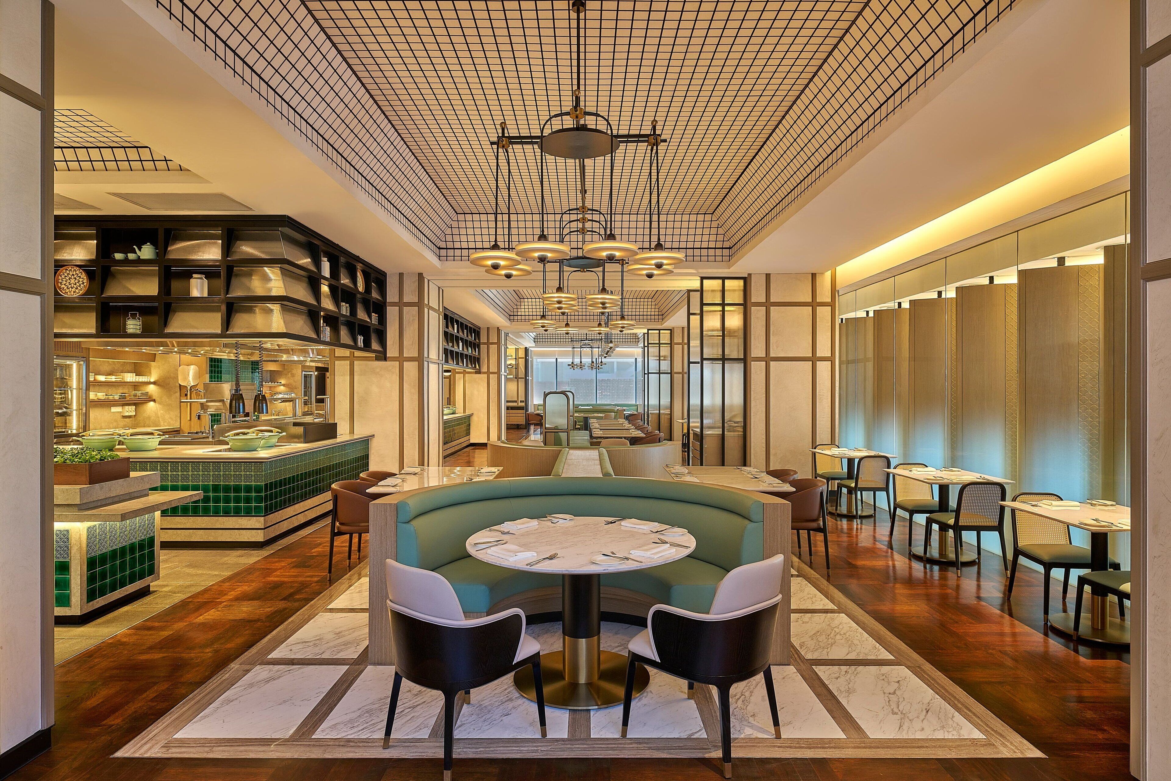 A modern hotel lobby with a central seating area, a bar, and a long dining section.