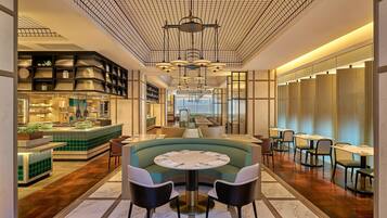 A modern hotel lobby with a central seating area, a bar, and a long dining section.