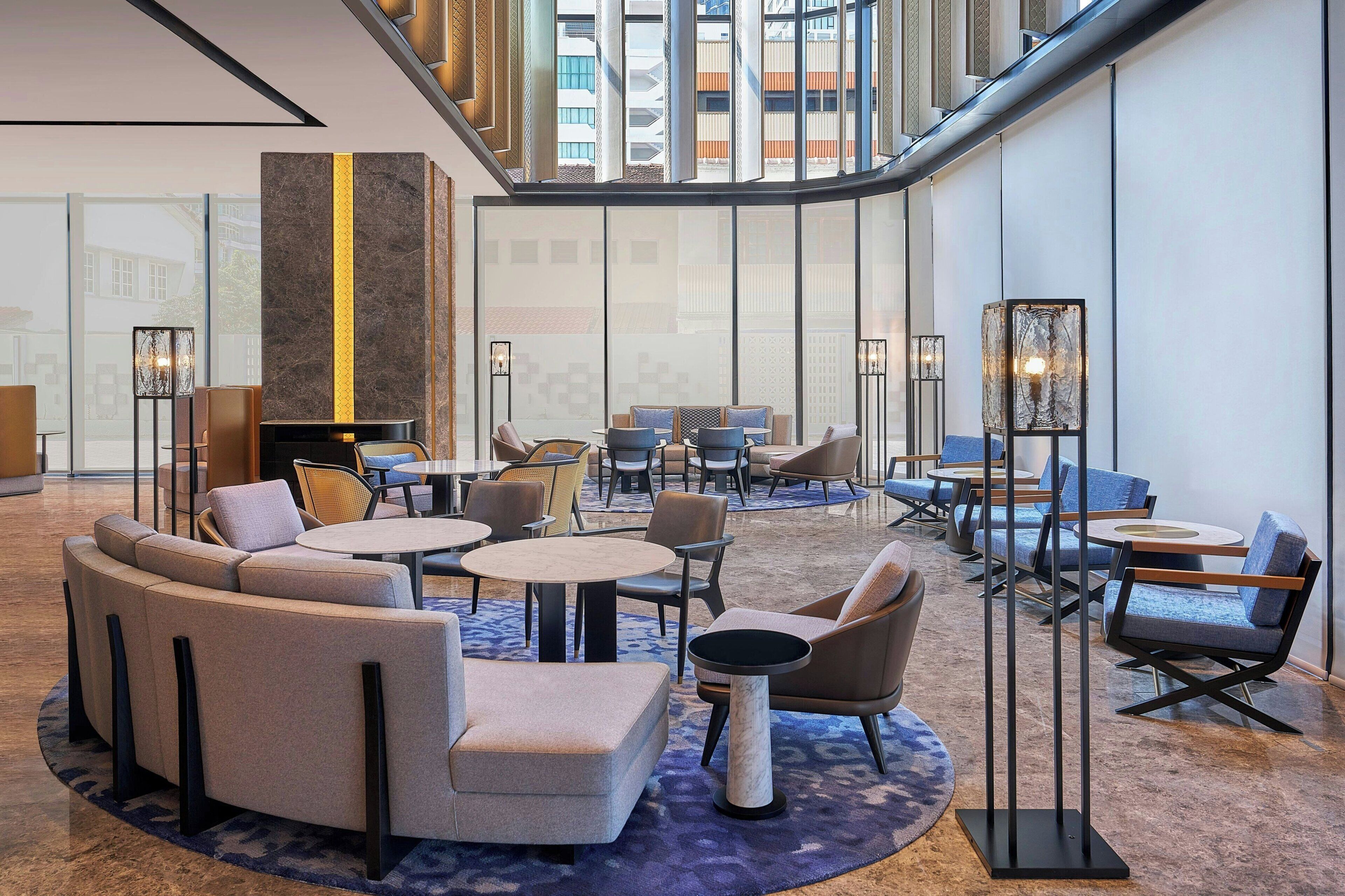 A spacious lobby with seating areas, a central column, and a view of the building's exterior through large windows.