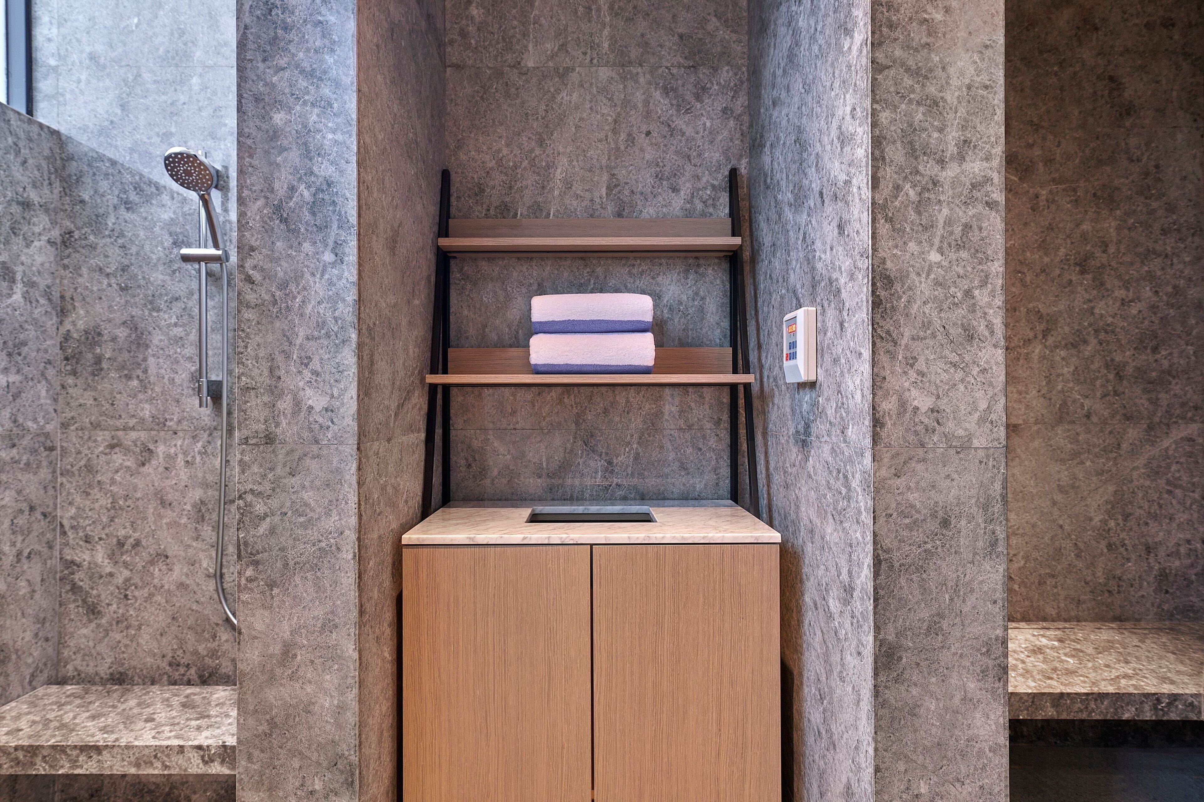 Een badkamer met een douche, een houten kastje en een plank met handdoeken.