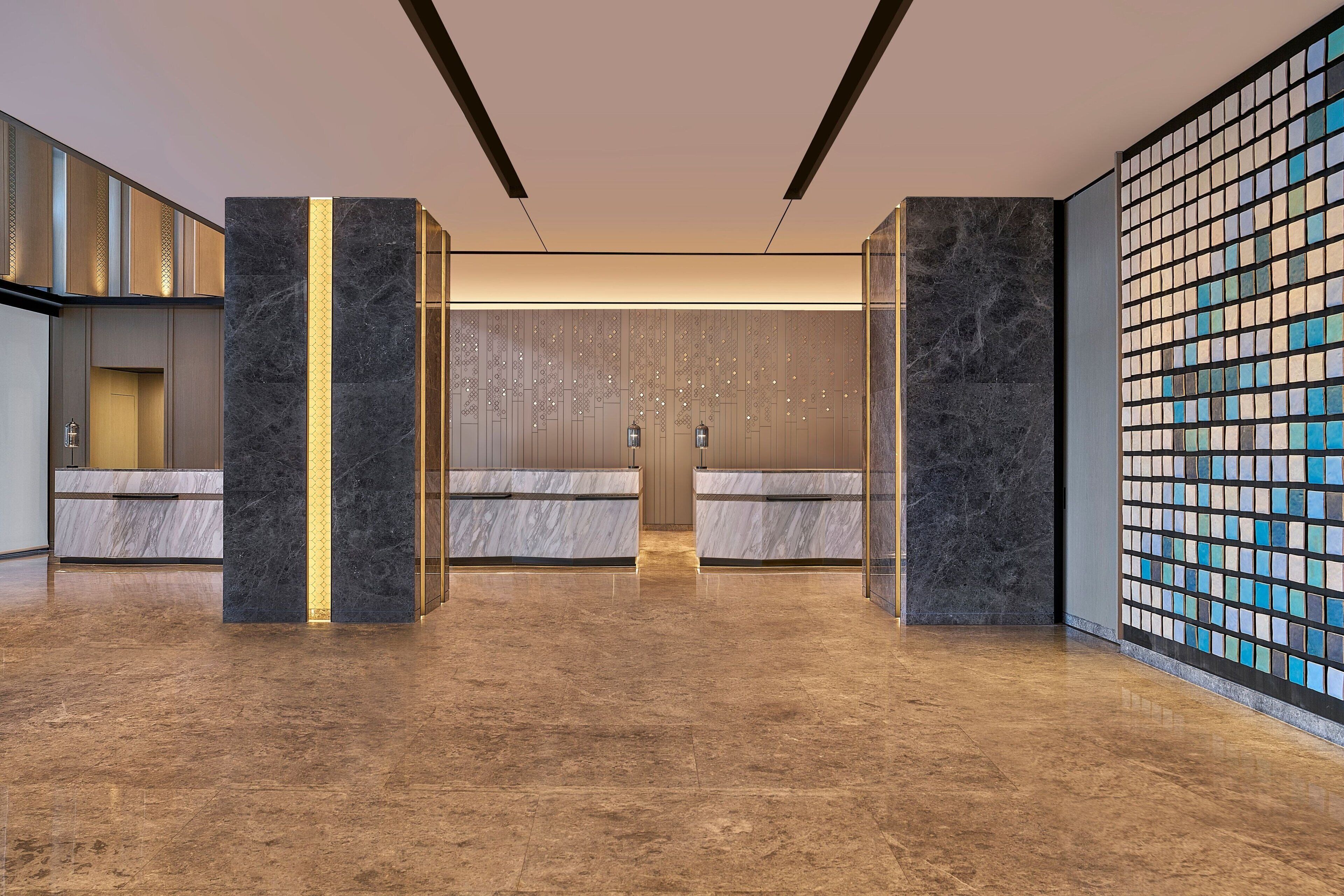 Een moderne lobby met marmeren vloeren, een receptiebalie en een decoratieve wand met een mozaïekpatroon.