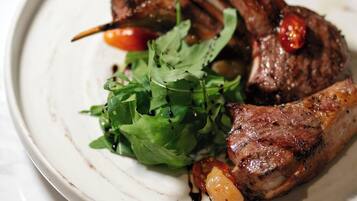 A plate with grilled meat, greens, and a cherry tomato.