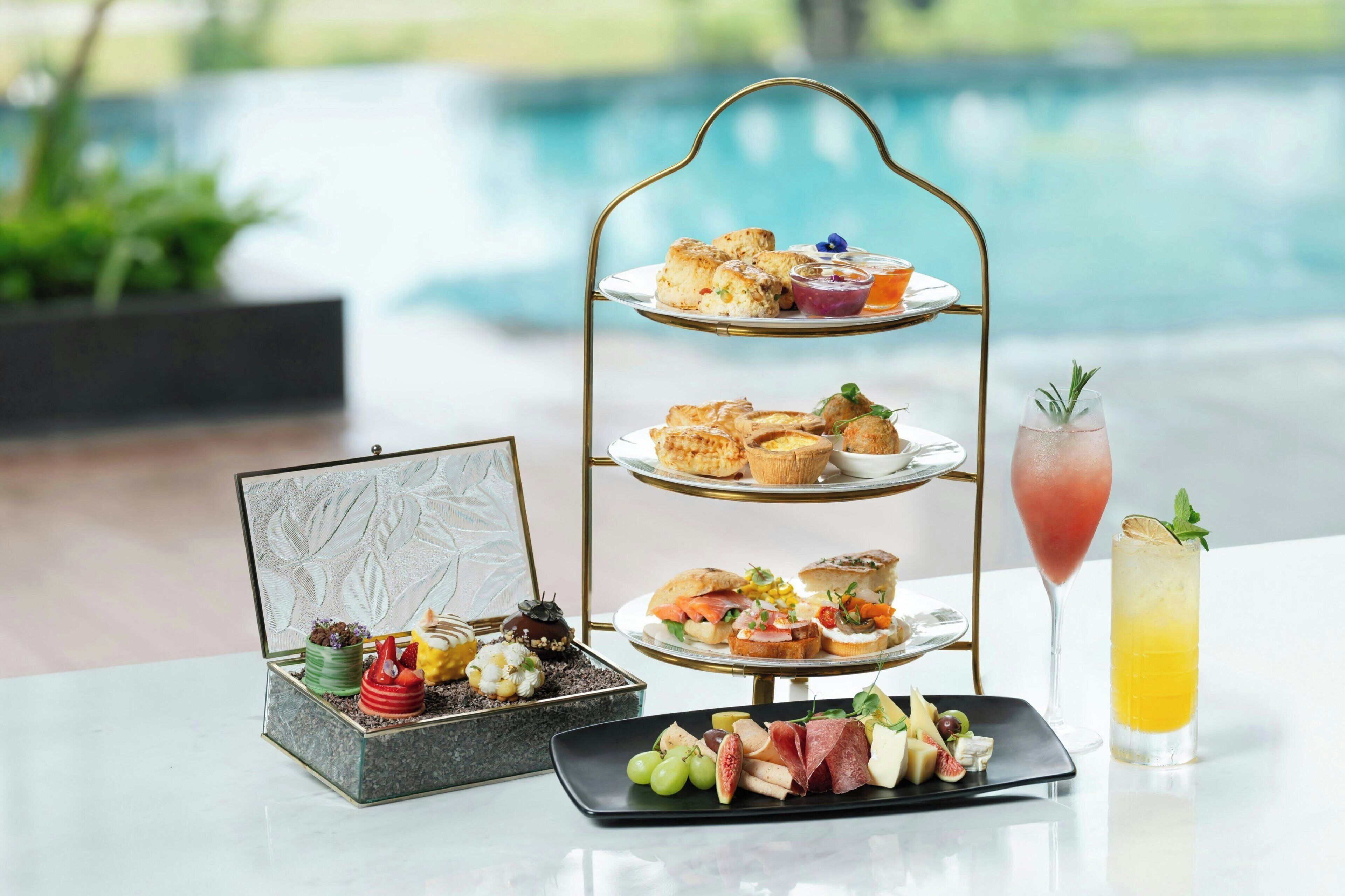 A tiered dessert stand with various pastries and a drink beside a pool.