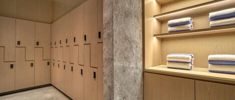 A modern bathroom with wooden lockers, a marble column, and shelves with folded towels.