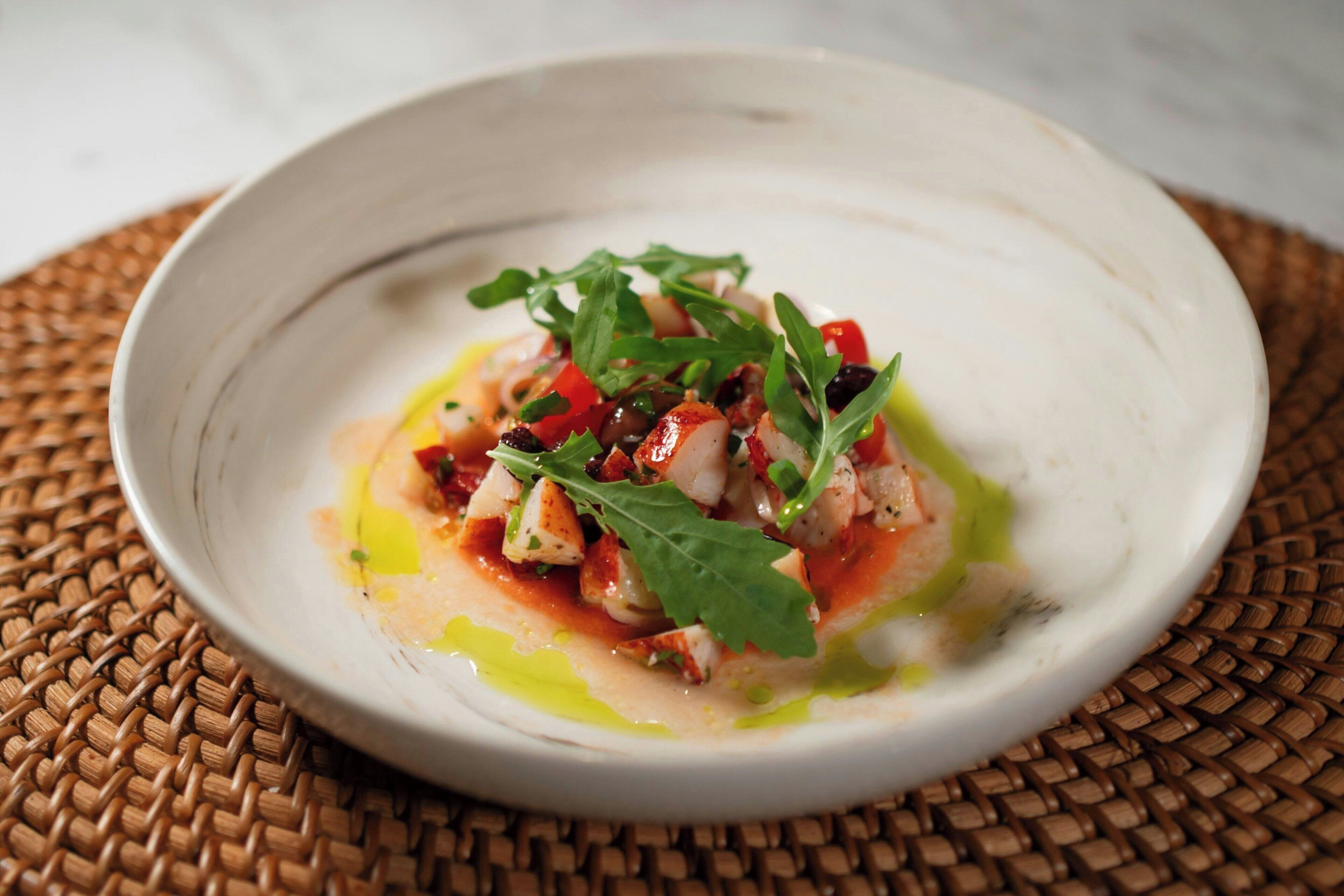 Une assiette blanche contenant un plat de fruits de mer, agrémenté de verdure, posée sur un tapis tressé.