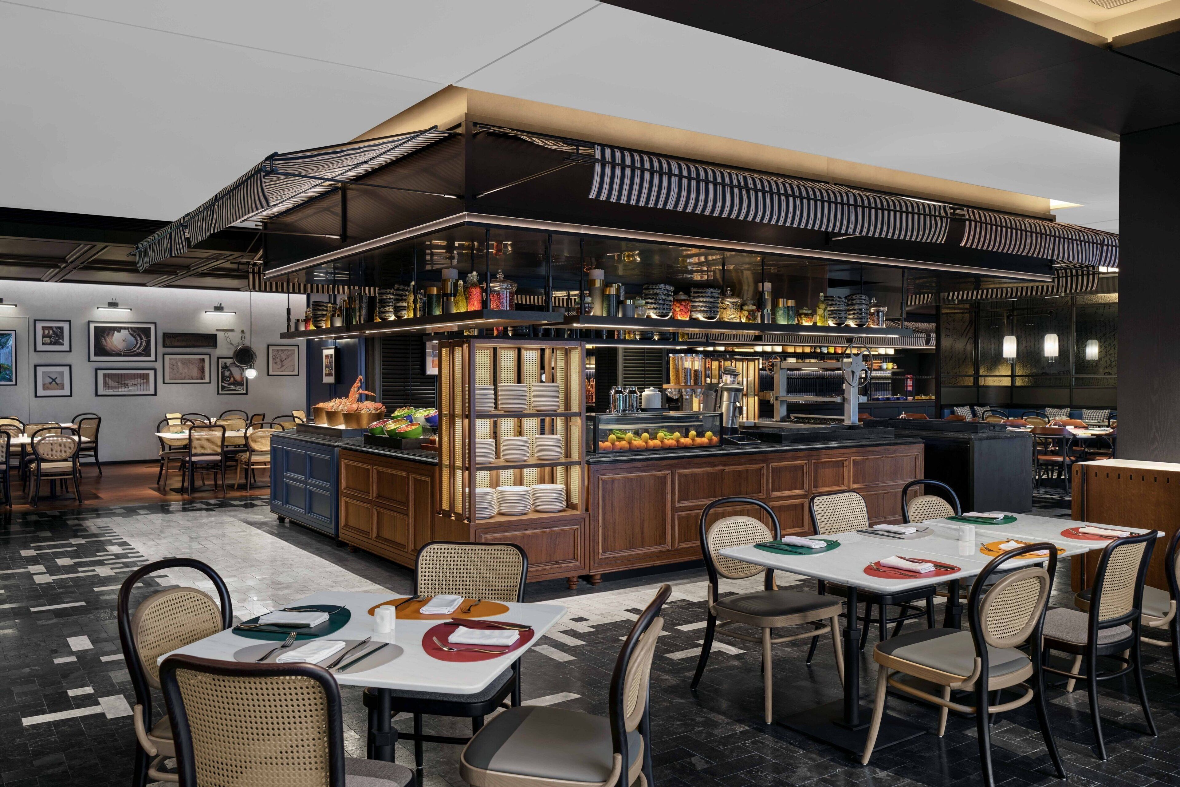 Un restaurante moderno con barra central, varias mesas para comer y diferentes opciones de asientos.
