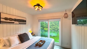 Ein Schlafzimmer mit Bett, Nachttisch, Fenster mit Blick ins Grüne und einem an der Wand hängenden Kunstwerk.