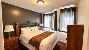 A bedroom with a bed, two bedside tables, a nightstand, a dresser, and a window with curtains. - 2 bedroom townhome with view of the mountain (Collingwood)