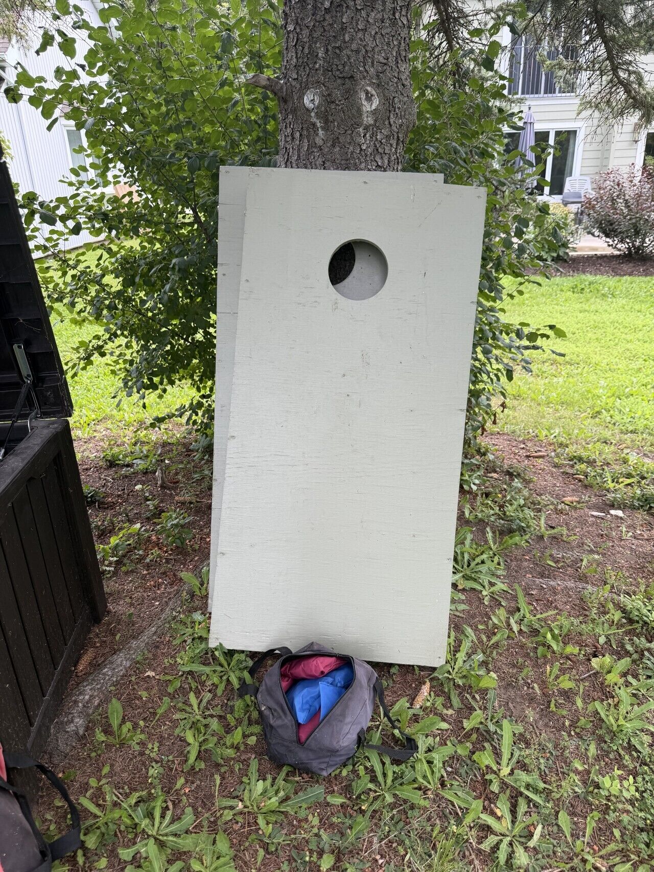 A white birdhouse attached to a tree, a black grill, and a gray bag on the ground.