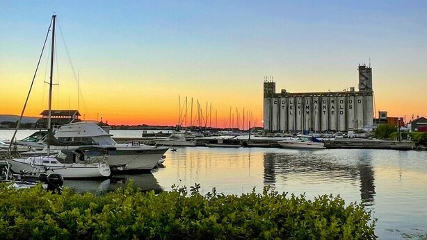 A marina with boats docked, a large industrial building, and a sunset in the background. - 2 bedroom townhome with view of the mountain (Collingwood)
