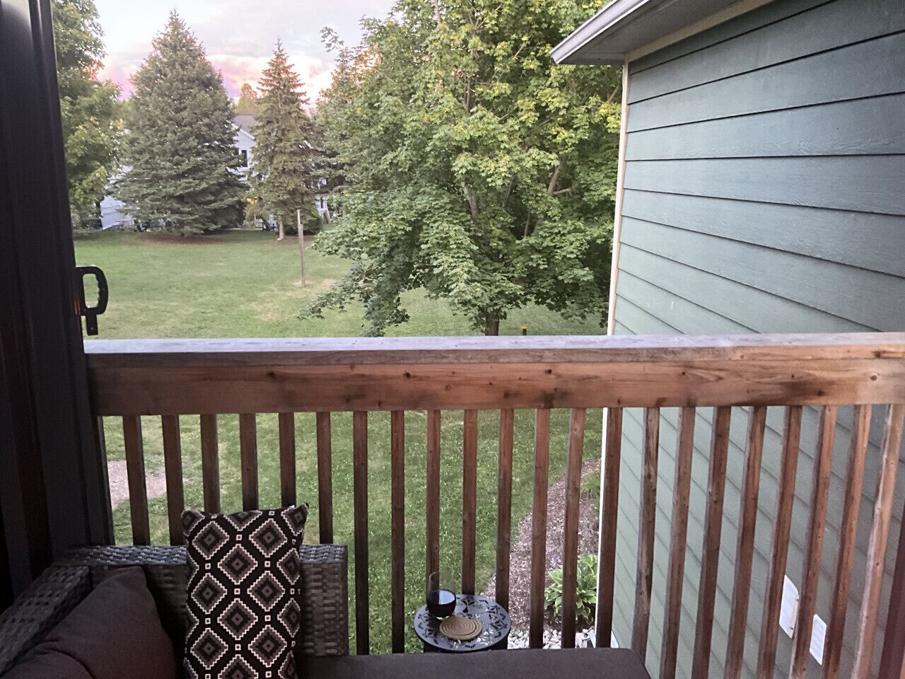 A wooden deck with a railing, a cushioned bench, and a patterned pillow.