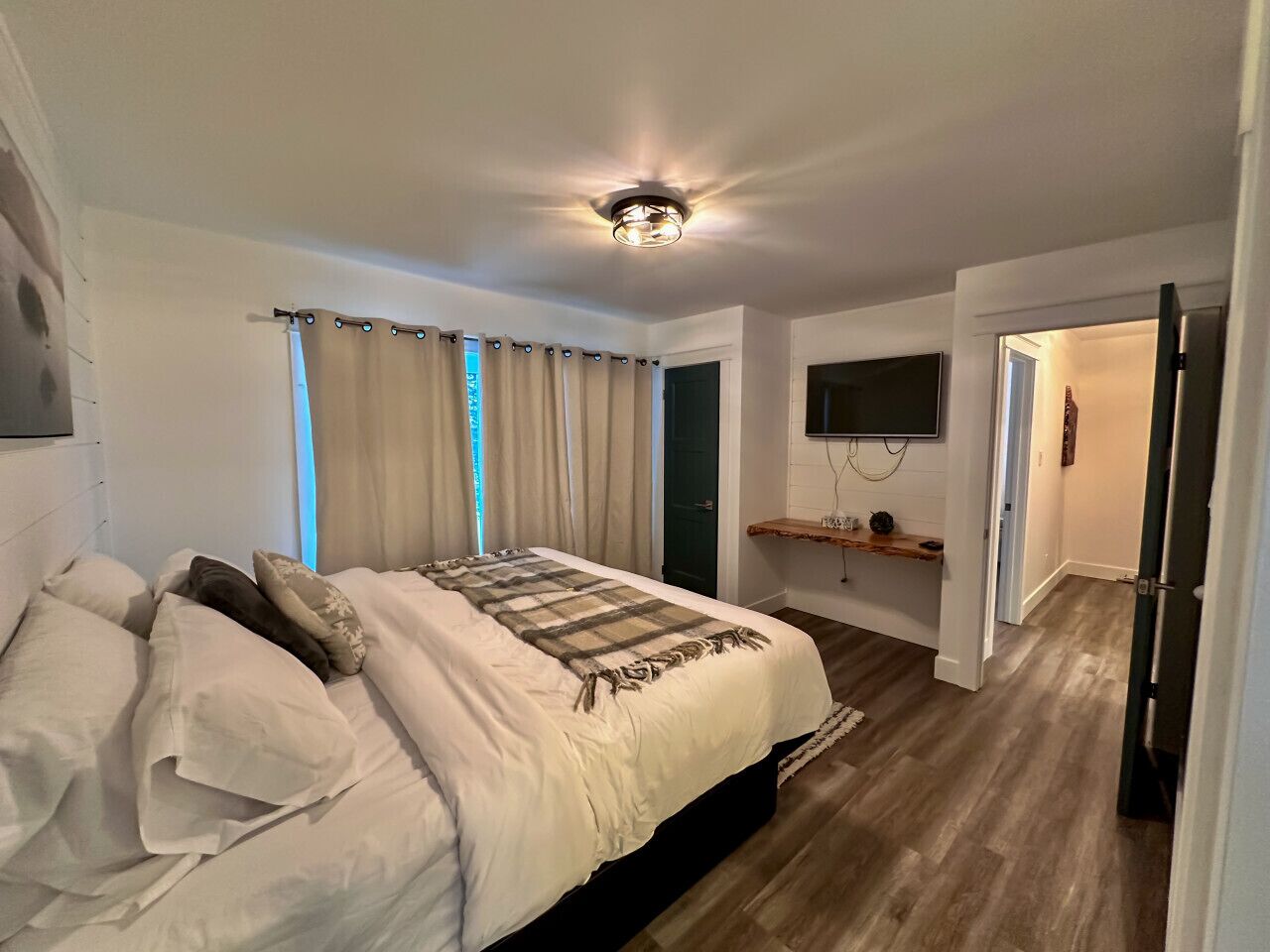 Une chambre à coucher avec un lit, des rideaux, un téléviseur fixé au mur et un plancher en bois.