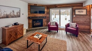 Una sala de estar acogedora con chimenea, paredes de madera y dos sillones rojos.