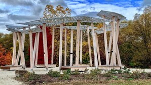 Un pabellón con una estructura geométrica distintiva en su techo, rodeado de árboles con follaje otoñal.