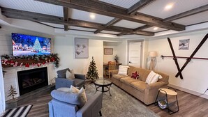 Uma sala de estar aconchegante com lareira, televisão, árvore de Natal e sofá.