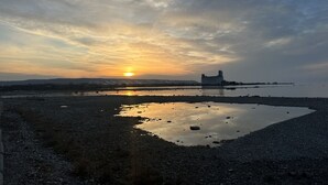 Pôr do sol sobre um corpo de água com um edifício ao longe.