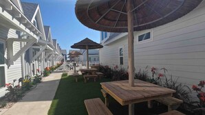 A row of white cabins with thatched umbrellas and wooden benches in a garden setting. - Paradise Palms - Walk to Beach! (Corpus Christi)