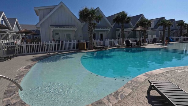 A swimming pool with a white fence, lounge chairs, and palm trees. - Paradise Palms - Walk to Beach! (Corpus Christi)