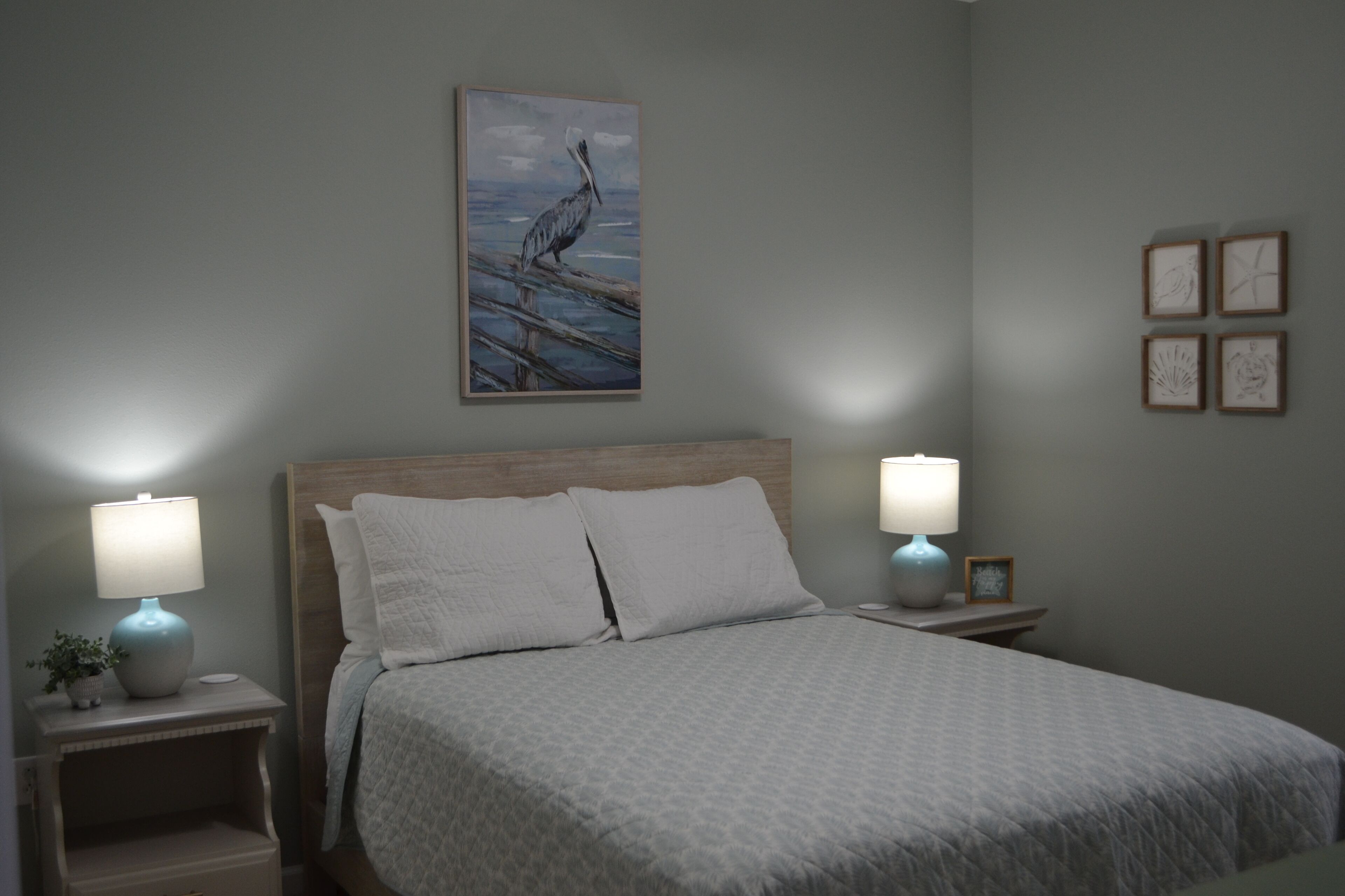 A bedroom with a bed, two bedside tables with lamps, a wall-mounted painting, and four framed pictures.