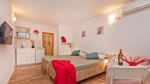 A bedroom with a bed, a desk, a chair, a microwave, and a small kitchen area. - BIS Studio Apartment 3 (Dubrovnik)