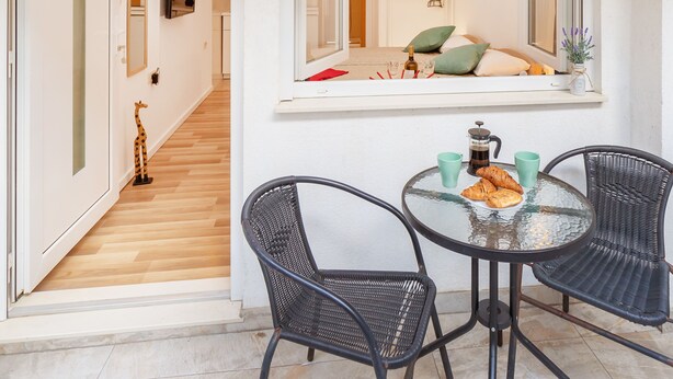 A dining area with a round glass table, two black wicker chairs, and a breakfast setting including croissants and a coffee pot. - BIS Studio Apartment 3 (Dubrovnik)