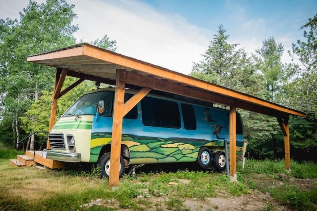 Un camping-car est garé sous un abri en bois, dans une zone boisée.