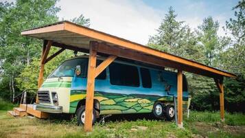 Un camping-car est garé sous un abri en bois, dans une zone boisée.
