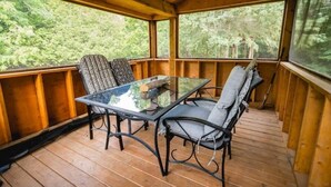 A wooden deck with a glass table and metal chairs, surrounded by wooden railings and a view of a forest. - Unique Glamping RV on 100 acres 1 hr from Toronto (Blackstock)