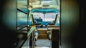 A narrow, enclosed space with a wooden ceiling and walls, a bench seat, a small table, and a window providing a view outside. - Unique Glamping RV on 100 acres 1 hr from Toronto (Blackstock)