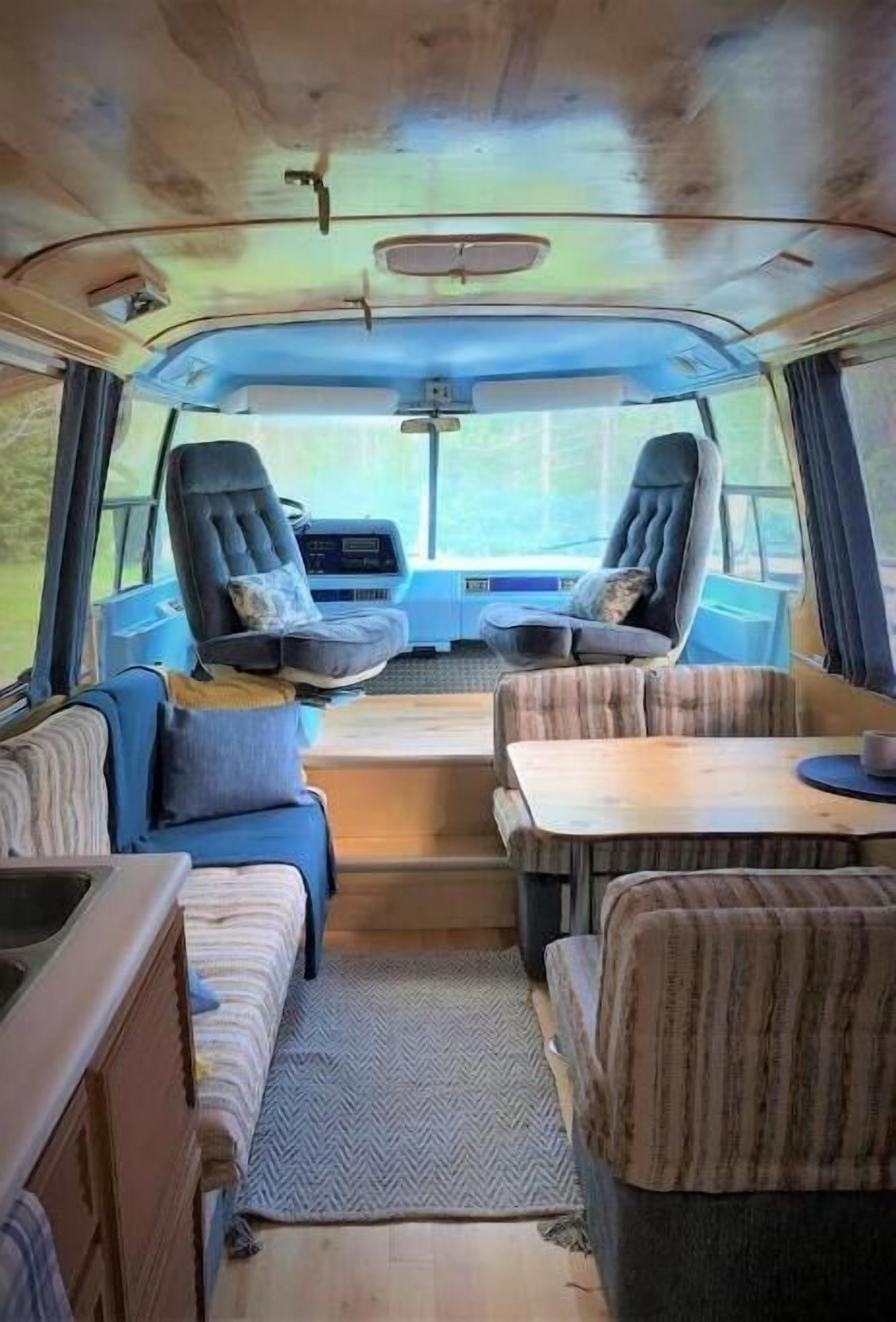Interior acogedor de una caravana, con una zona de estar central, una mesita y un rincón de cocina.
