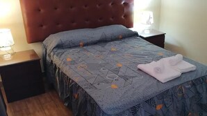 Siististi pedattu sänky, jossa on kuviollinen päiväpeite ja oikealla puolella taitettu pyyhe.