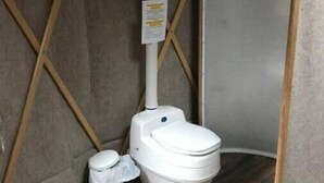 Une petite salle de bain fermée, avec des toilettes blanches, une poubelle et un panneau sur le mur.
