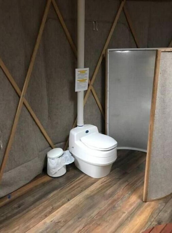 Une petite salle de bain fermée, avec des toilettes blanches, une poubelle et un panneau sur le mur.