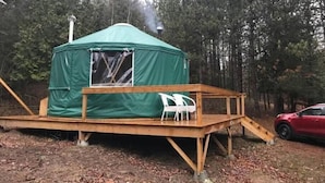 Une tente verte avec une terrasse en bois et une rampe, entourée d’arbres.